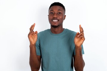 young handsome man wearing green T-shirt over white background holding fingers crossed with worried expression hoping boss didn't noticed mistakes at work.