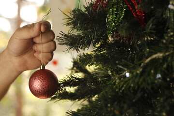 Mano colocando una esfera roja al &aacute;rbol de Navidad 