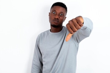 young handsome man wearing grey sweater over white background looking unhappy and angry showing rejection and negative with thumbs down gesture. Bad expression.