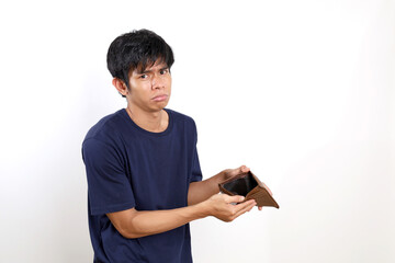 Disappointed young asian man standing while opening his empty wallet. Isolated on white background