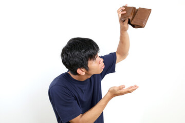 Disappointed young asian man standing while opening his empty wallet. Isolated on white background