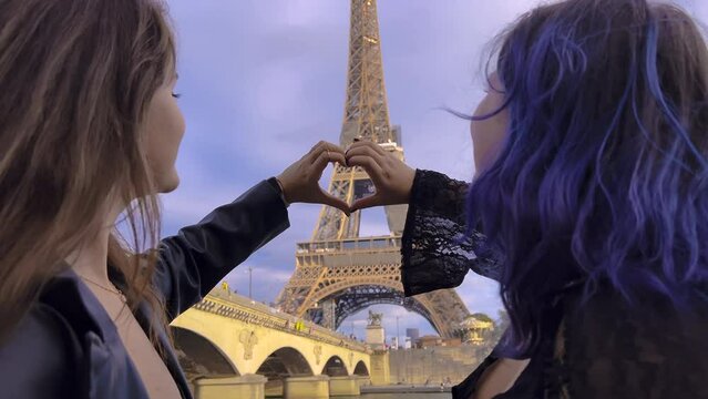 The hands of two girls make a heart sign on the background of the Eiffel Tower. Young couple travel in Paris
