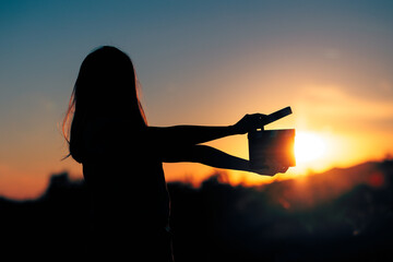 Silhouette of a Woman Holding a Cinema Clapperboard in the Sunset. Producing director with film slate making a movie outdoors
