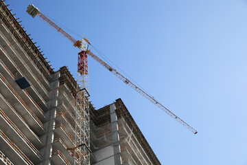 Construction site with tower crane near unfinished building, low angle view