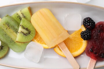 Delicious popsicles, ice cubes and fresh fruits on plate, top view