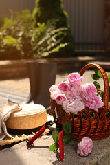 Fototapeta na wymiar Basket of beautiful tea roses, straw hat and gardening tools outdoors