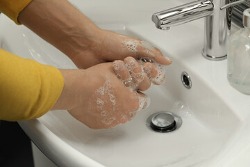 Man washing hands with soap over sink in bathroom, closeup