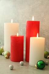 Burning candles with Christmas baubles on light grey table