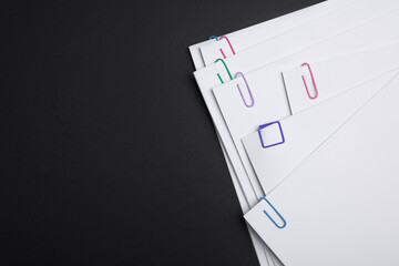 Sheets of paper with clips on black background, top view. Space for text