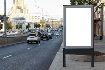 White blank vertical billboard in the city. Evening, urban highway with traffic flows. Mock-up.