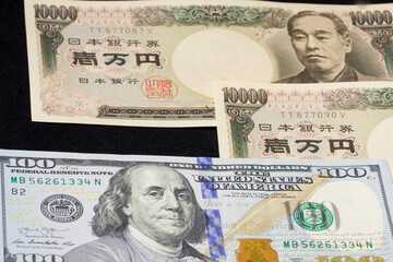 US $100 dollar bill on a sheet of many 10,000 JPY bills. Travel and foreign money exchange concept. Captured in October 2022. 