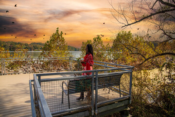 an African American woman with long sisterlocks wearing an orange dress standing on a wooden platform on the banks of the Tennessee River surrounded by autumn colored trees and lush green trees - Powered by Adobe