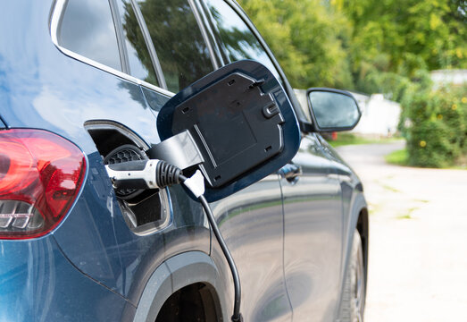 Rear view of electric car with buildings in the background showing charge cable plugged in and charging the car with a granny cable
