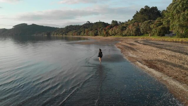 Aerial drone view of girl running Cornwallis beach in Auckland, New Zealand, following shot