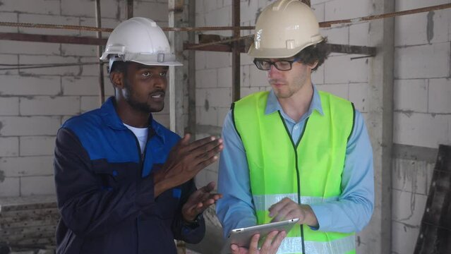 Team architect two young man discussing and looking digital tablet for inspection construction site, foreman and worker examining infrastructure of house development for planning project together.