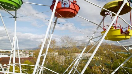 Aerial around view of the city ferris wheel with bucket seat in the golden autumn amusement park under light blue cloudy sky, drone flying inside