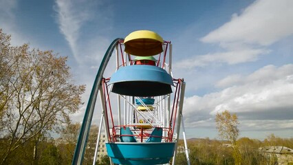 Aerial around view of the city ferris wheel with bucket seat in a golden autumn amusement park under light blue cloudy sky, drone flying inside