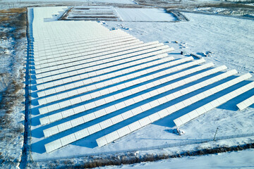 Aerial view of snow covered sustainable electric power plant with rows of solar photovoltaic panels for producing clean electrical energy. Low effectivity of renewable electricity in northern winter