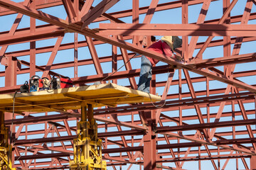 An electric welder works at a height, inside the metal structures of the future building.