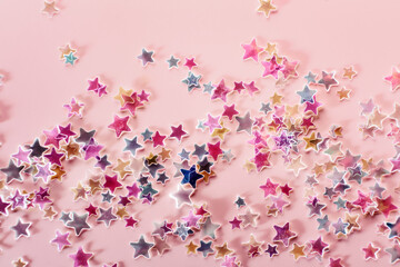 Pink, blue and yellow holographic Stars Glitter Confetti on pink background. Festive backdrop