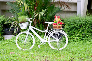 Fototapeta na wymiar Many colors of fake flowers in the basket on a white bicycle in the park with natural background at Thailand.
