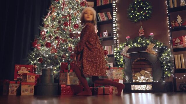 Little girl sneaks on tiptoe to the Christmas tree turns around and while no one sees takes a gift