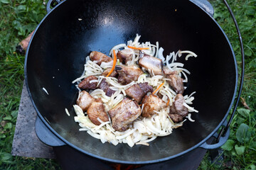 Pilaf. Cooking step by step. Step 3. Cooking meat wih onion in a cauldron. Pork is fried in oil over a fire. 