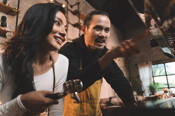 happiness two waiter teaching woman with apron to use a coffee machine for make a coffee. the happiness men and woman in bakery small business on waiter and waitress uniform.