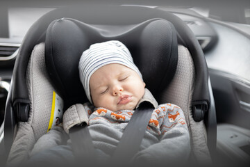 Cute little baby boy sleeping strapped into infant car seat in passenger compartment during car...