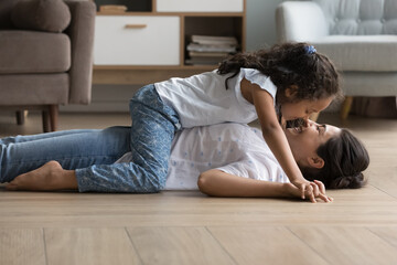 Fototapeta premium Loving Indian mother her little adorable tender daughter feeling love while touch noses spend time together at home lying on warm floor in cozy living room, family enjoy communication, express caress