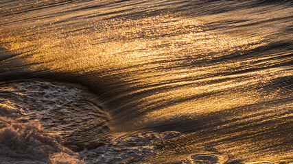 Ripple sea ocean water surface with golden sunset light. Sea waves close up