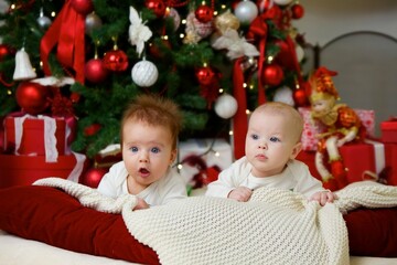 Two babies are lying in a festive outfit on the background of New Year and Christmas decorations. The concept of holidays