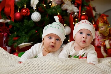 Two babies are lying in a festive outfit on the background of New Year and Christmas decorations. The concept of holidays