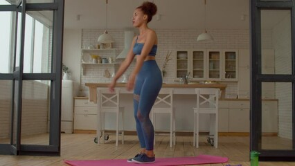 Determined attractive sporty fitness African female exercising reverse lunges, flexing leg muscles and strengthening quads, glutes, and hamstrings while practicing sports training in domestic room.
