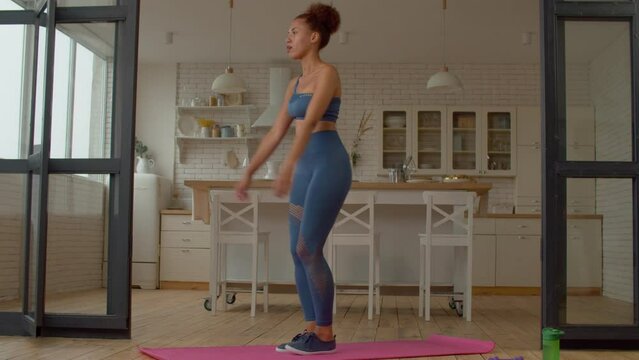 Determined attractive sporty fitness African female exercising reverse lunges, flexing leg muscles and strengthening quads, glutes, and hamstrings while practicing sports training in domestic room.