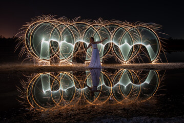 Woman posing for light painting with bright lights in the dark. Reflection in the water
