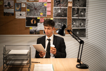 Detective working at desk in his office, drinking coffee and analyzing materials