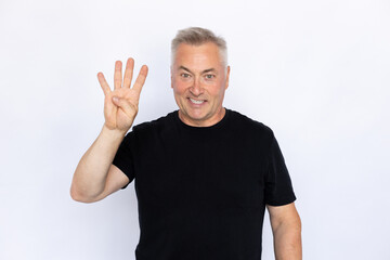 Naklejka premium Portrait of happy senior man showing four fingers. Excited Caucasian male model in black T-shirt with gray hair looking at camera, smiling while counting. Countdown concept.