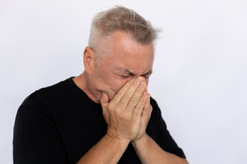 Fototapeta premium Senior man sneezing close up. Male model in black T-shirt covering face with hands, sneezing in hands with closed eyes. Portrait, studio shot, cold concept