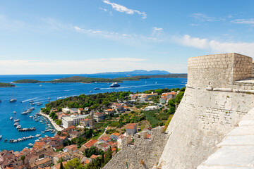 The wall of the Spanish Fortress in Hvar looking down at a part of the town with boats and islands in the Adriatic Sea.