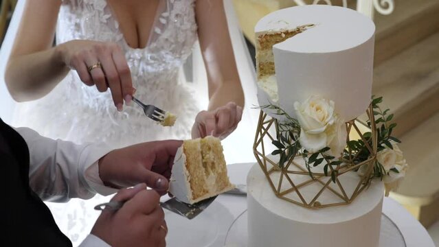 The bride and groom cut off a piece of the wedding cake and put it on a plate.