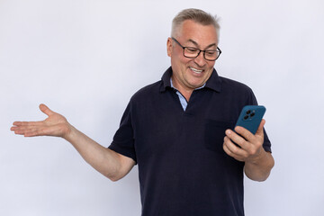 Senior man spreading arm. Male model in blue polo shirt shrugging, being uncertain, looking at smartphone with smile. Portrait, studio shot, uncertainty concept