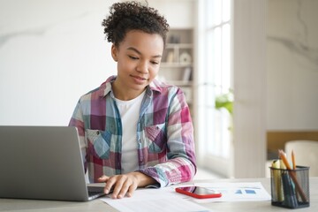 Mixed race teen girl student learning at laptop look on mobile phone, read message in social network