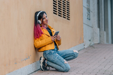 urban girl on the street sitting listening to music with headphones and mobile phone