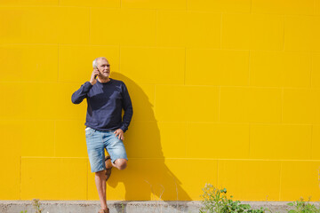 mature man talking on mobile phone on yellow wall