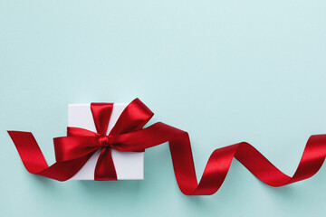 Gift or present box with red bow ribbon on light blue table top view. Greeting card for Christmas, birthday or New Year.