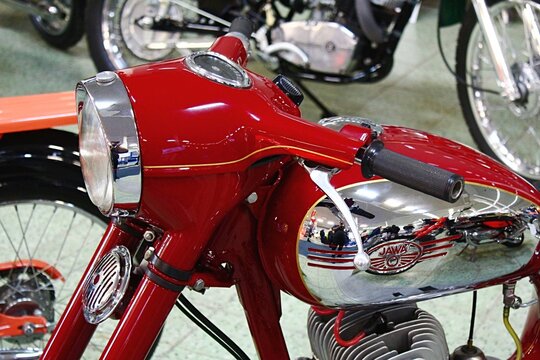 Round headlight and handlebars of red veteran Czechoslovak motorcycle Jawa 350, called Panelka (concrete lady), from year 1967, displayed on car expo in Nitra, Slovakia in veteran hall. 