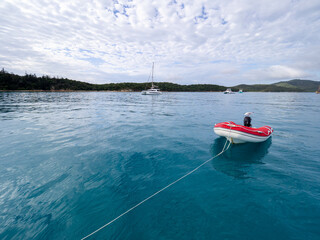 Red dinghy trailing by a rope in blue water