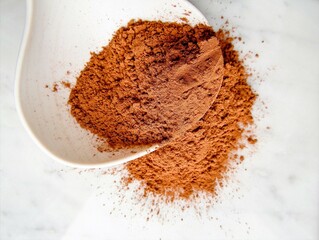 cocoa powder in a spoon on a light marble background