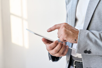 Male hands of old senior professional businessman wearing suit holding digital tablet device working using online business smart technology corporate fintech modern applications, closeup.